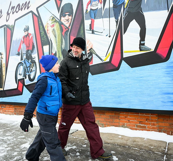 Father and son in snowsuits talking and walking by a brick building with a Hayward sign on it