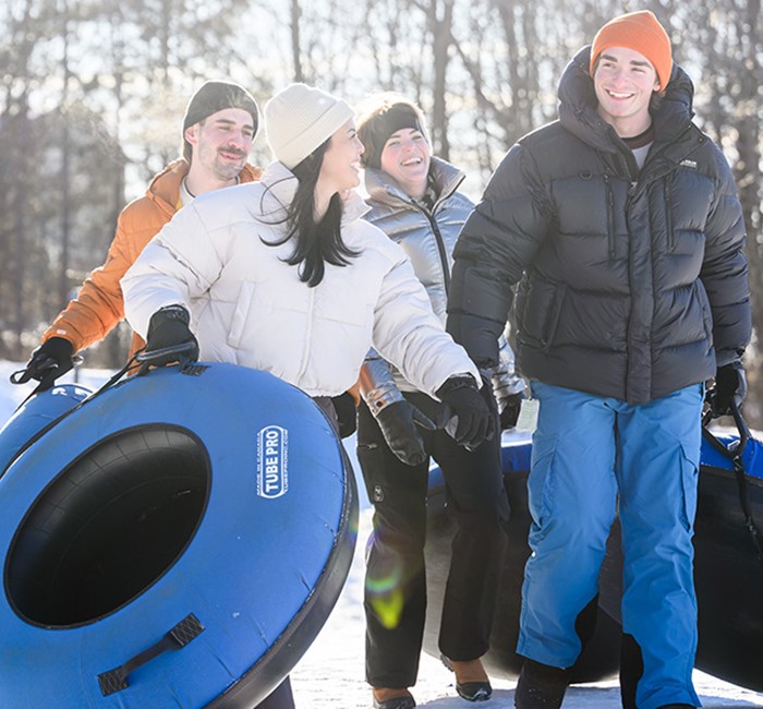 Friends in snow suits carrying snow tubes