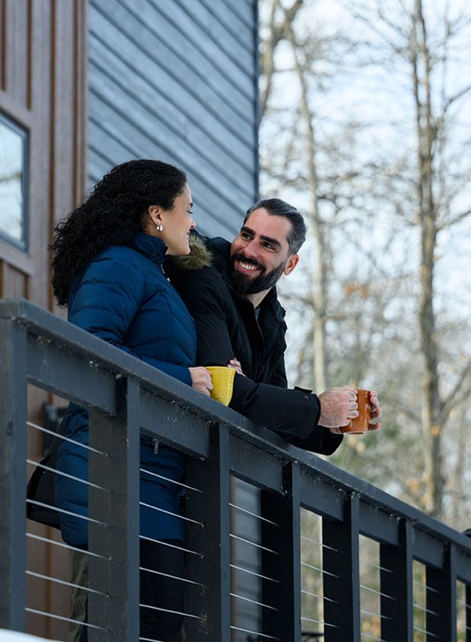 Couple drinking coffee on a balcony outside of a house in the woods