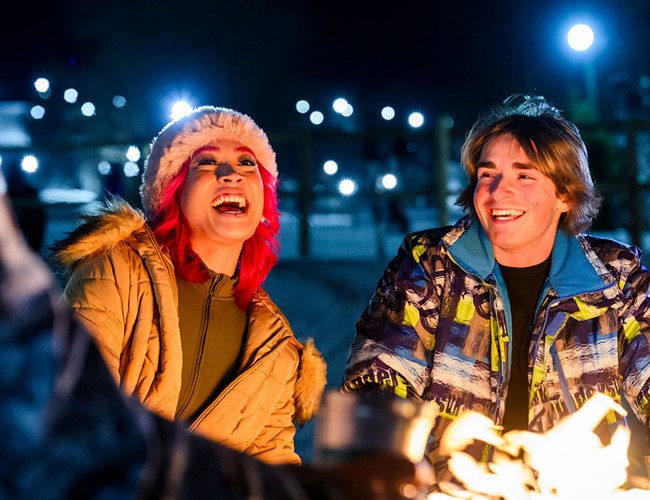 Friends laughing around a fire, outside at night